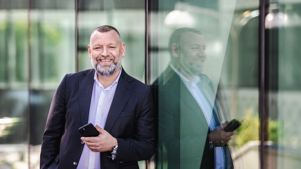 Andreas har en telefon i handen och lutar sig mot fönster på en kontorsbyggnad där han speglas i glaset.